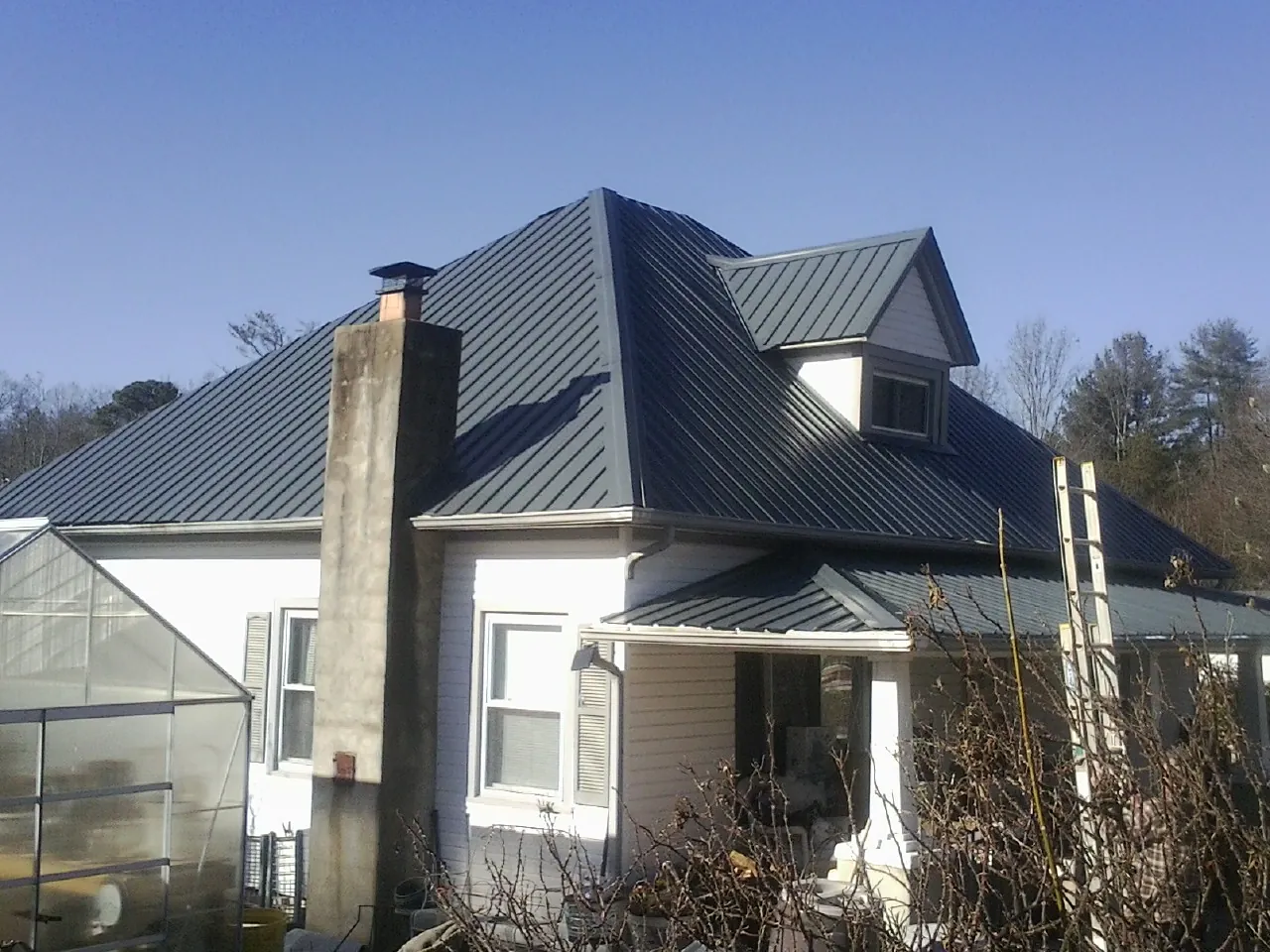 Dark blue standing seam metal roof on a white farmhouse with dormer — Slate & Tile Roof Repair by Roofing Brothers in Penhook