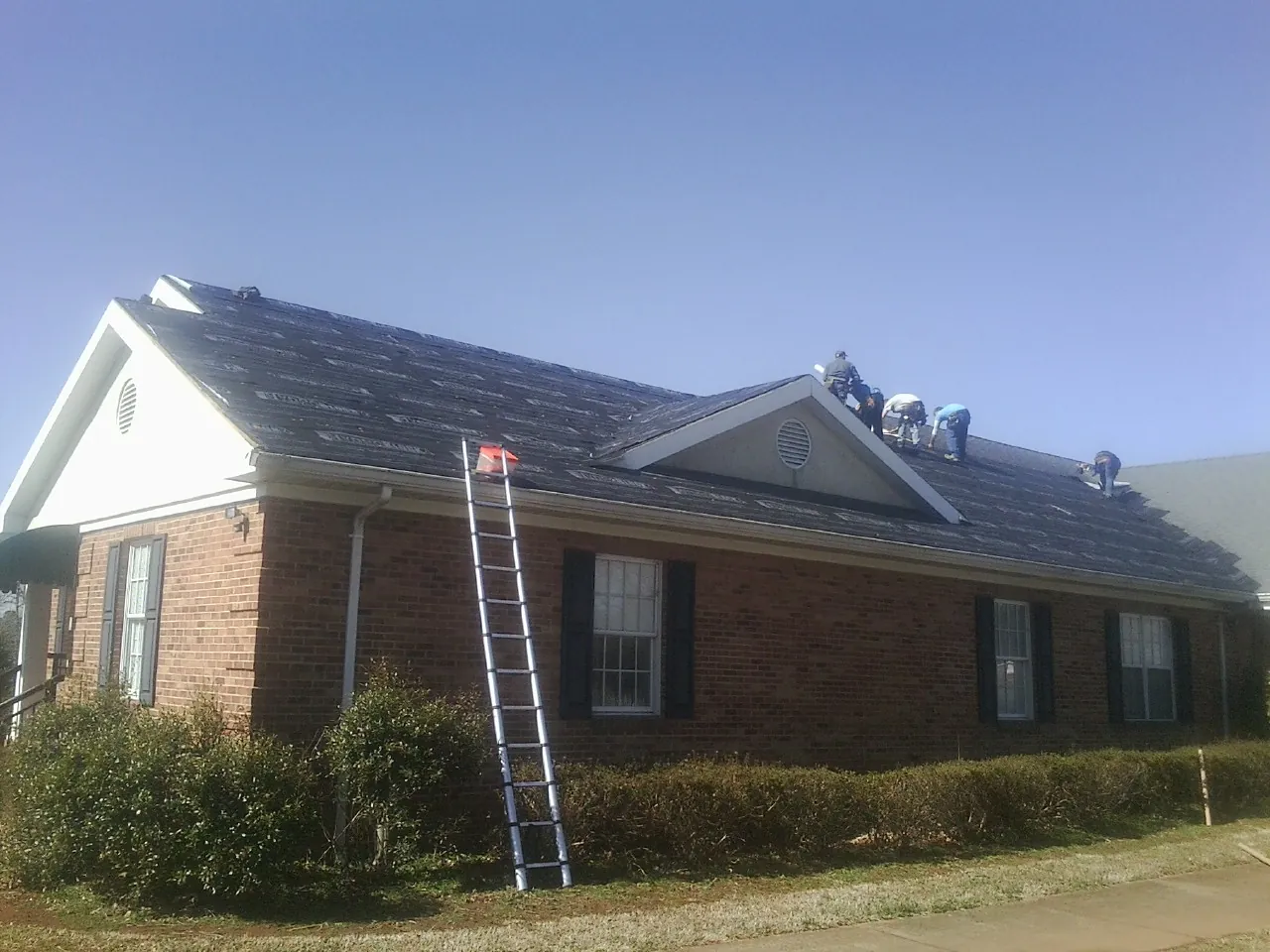 Crew tearing shingles off a brick ranch roof with a ladder set — Emergency Roof Repair work by our crew in Penhook