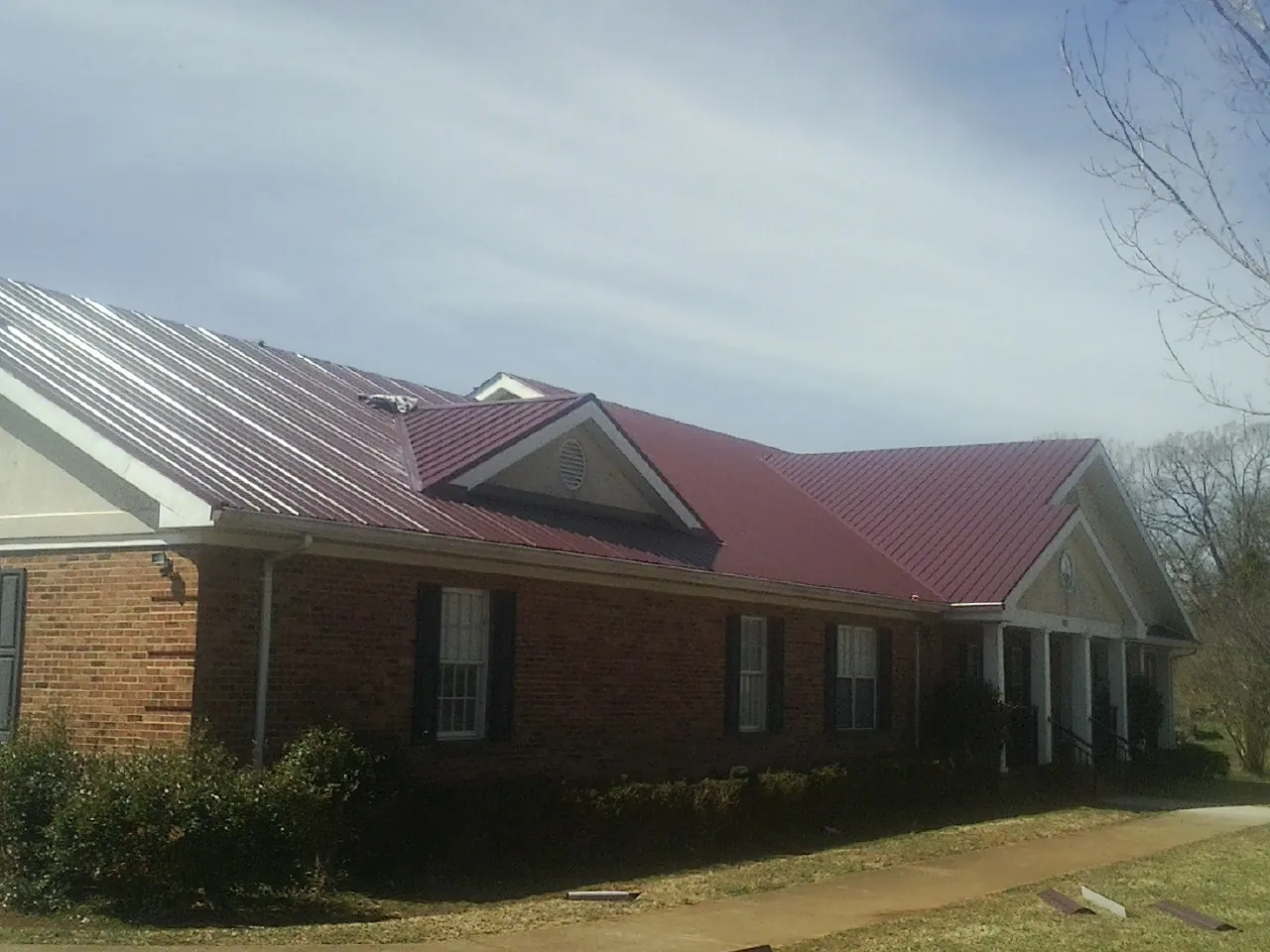 Red metal roof with gabled entries on a long brick building, from a Hail Damage Roof Repair job in Penhook