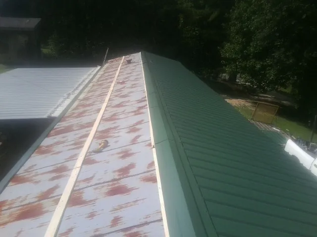 Old rusted panels beside newly installed green metal roofing — Wind Damage Roof Repair by Roofing Brothers in Penhook