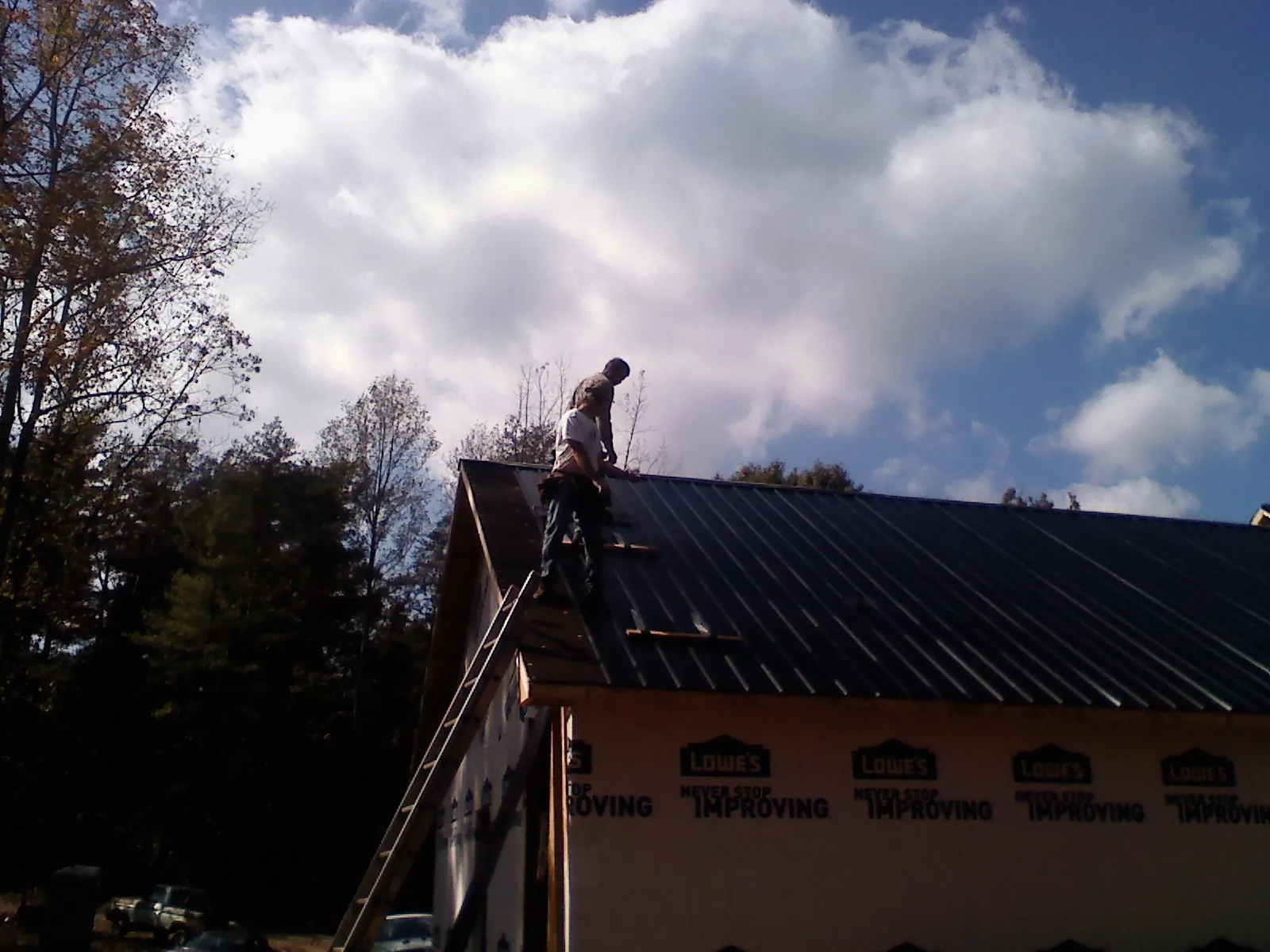 Roofer fastening dark metal panels high against a cloudy sky, from a Roof Inspection job in Penhook